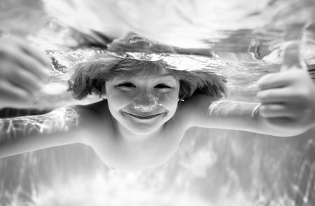Funny kids face under water. Children playing in swimming pool. Kid swimming underwater in pool. Blue sea water. Child boy swimming in sea.の写真素材