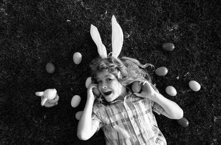 Easter bunny children with rabbit ears in garden hunt egg. Child hunting eggs, wear bunny ears hold Easter eggs. Top view funny kids face.の写真素材