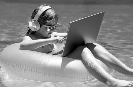 Business summer travel. Happy little boy learning online computer laptop. Kid relax on floating ring using computer in swimming pool. Summer business and technology.の写真素材