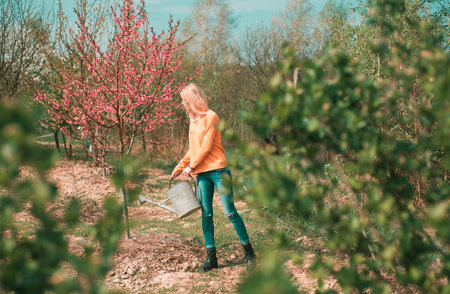 Happy young woman gardener spraying water on plants. Hobby concept. Girl gardening on spring garden.の写真素材