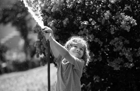 Child playing with garden hose in backyard. Funny excited kid having fun with spray of water on yard...