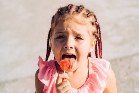 Little girl lick lollipop. Lifestyle portrait of funny kid outdoors. Summer kids outdoor portrait. Close up face of cute child. Kid having fun outdoor on sunny summer day.の写真素材
