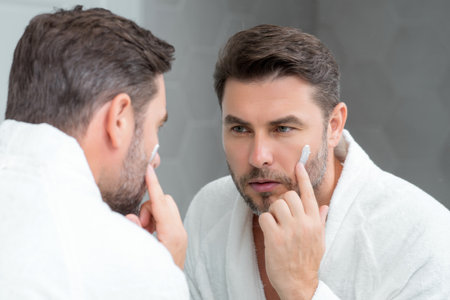 Beauty male face cream. Beauty routine. Beauty man with perfect skin. Anti-aging and wrinkle cream. Concept of male beauty. Close-up face of man applying cream to skin. Skincare cosmetics concept.の写真素材