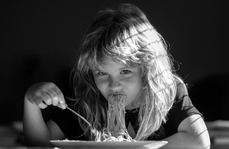 Child eating on blurred background. Hungry little boy eating. Home food for kids. Tasty food, messy child eating spaghettiの写真素材