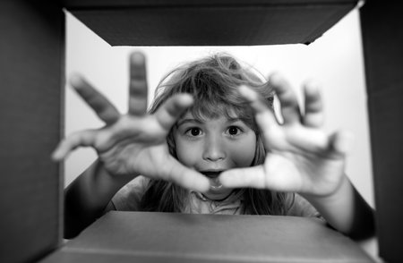The surprised child unpacking, opening carton box and looking inside. The package, delivery, surprise, kids gift concept. Parcels and delivery. Shocked kids, amazed kids emotions, wow.の写真素材