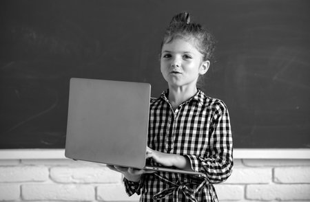 Portrait of attractive cheerful pupil girl using laptop. Kids education, school technology.の写真素材