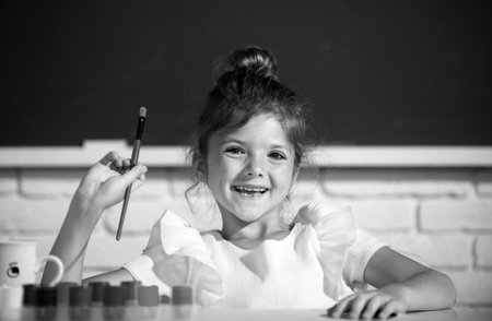 Child girl draws in classroom sitting at a table, having fun at school blackboard background. Painting school lesson, drawing art.の写真素材