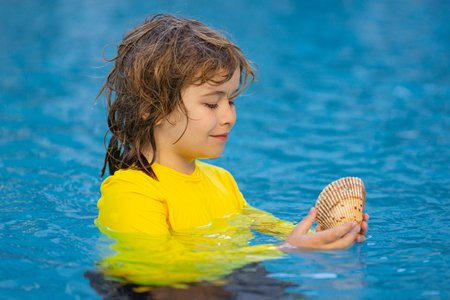 Portrait of little kid holding seashells and dreaming about summer vocation. Cute child playing with shell outdoor on summer beach. Little boy holding a sea shell. Summer vacation concept.の写真素材