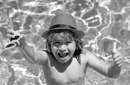 Kid boy swimming in pool play with floating ring. Smiling cute kid in sunglasses swim with inflatable rings in pool in summer day. Child relax with pool ring in beach sea water.の写真素材