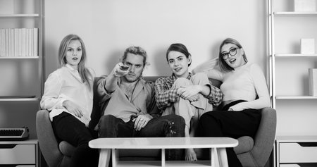 Youth group. Friends watching TV in evening at home. Group of young people sitting on sofa and...