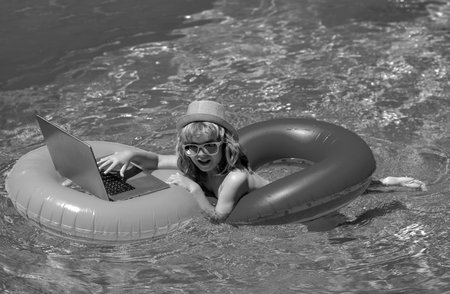 Summer office and freelance concept. Child sitting in swimming ring in pool and using laptop. Shopping online, freelance concept, summer travel.の写真素材