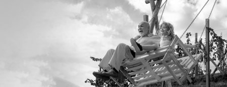 Old grandfather and young child grandson swinging in garden outdoors. Grand dad and grandson sitting...