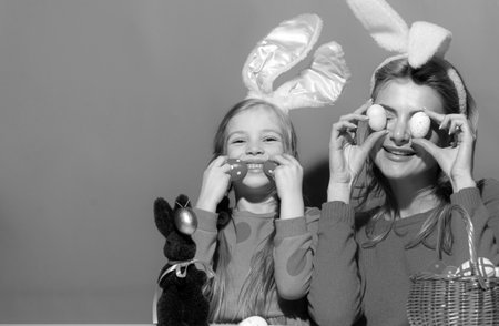 Portrait of mother with daughter wearing rabbit ears with decorating Easter eggs isolated on blue.の写真素材