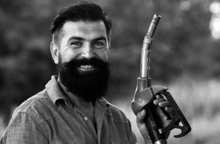 Man on petrol pump filling nozzles. Gas station. Portrait of bearded man hold fueling nozzle...