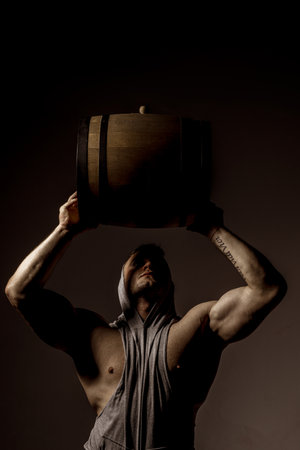 Strong man hold wooden barrel on black. Oktoberfest. Brewer man. Muscular man. Brewery concept. Beer for pub and bar. Oak barrels, keg. Man carries wooden barrel. Barrel with whiskey.の写真素材