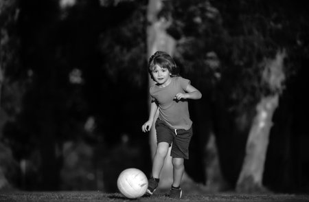 Boy child playing football on football field. Kid playing soccer. Child soccer player in park.の写真素材