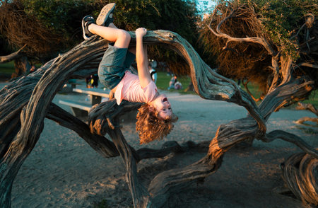 Kid climbing tree. Caucasian boy happily lying upside down in a tree hugging a big branch.