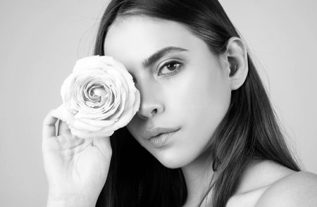 Studio portrait of young beautiful woman with roses. Close-up portrait of a beautiful young girl with a pink rose near face.の写真素材