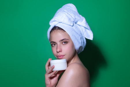 Beauty portrait of a beautiful half naked woman applying face cream isolated on studio background....