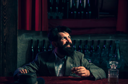 Handsome bearded man enjoying whiskey in bar. Hipster drinking a brandy in bar.