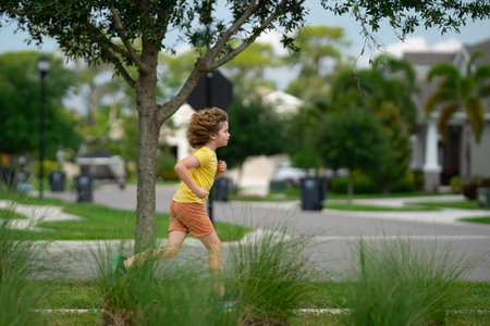 Kid running in summer street. Child enjoy run. Little boy running on neighborhood street. Kids run on american city running road. Child boy running in park. Sports and fitness, run exercise for kids.の写真素材
