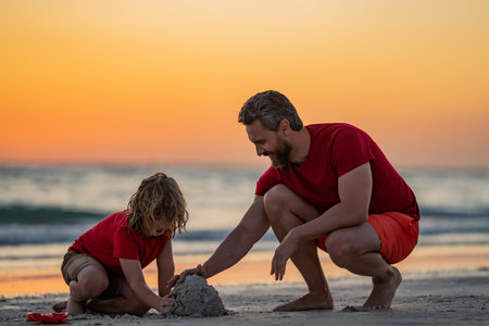 Summer family. Kid and father building sandcastle. Father and son playing on summer beach. Father and child son playing in the sand on summer tropical beach on sunset. Sand castle on summer beach.の写真素材