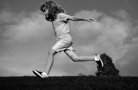 Child fun run outdoors. Kid playing in summer park. Little boy running on green fresh grass field.の写真素材