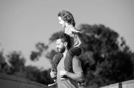 Daddy piggyback his little son outside. Handsome father piggybacking son playing on nature, dad holding riding on back adorable cheerful kid boy enjoy active game.の写真素材