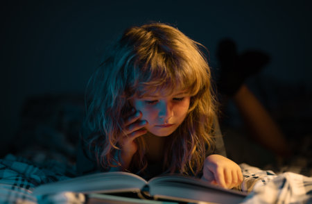 A little cute boy reading a book lying on the bed. Child reading a book on bedtime night. Kids development of the imagination.の写真素材