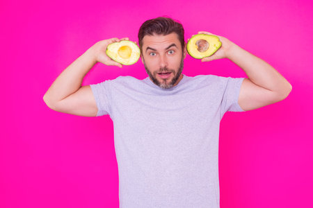Man hold half of fresh avocado isolated on pink background, studio portrait. The avocado. Healthy...
