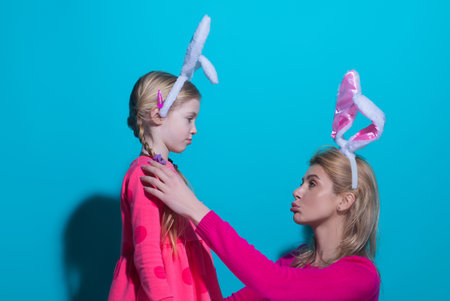 Happy Easter. A mother and her daughter painting Easter eggs. Happy family preparing for Easter. Cute little child girl wearing bunny ears on Easter day.の写真素材