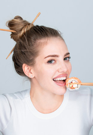 Beautiful girl eating japanese sushi rolls with chopsticks, order in fastfood restaurant. Beauty woman holding sushi with chopsticks.の写真素材