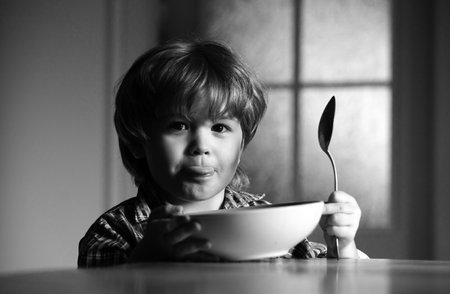 Baby eating food on kitchen. Cute kid are eating. Laughing cute child baby boy sitting in highchair and eating on blurred background.の写真素材