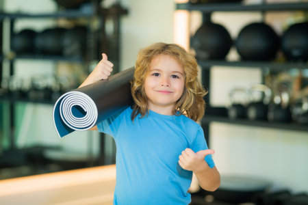 Fit kid holding yoga mat in gym. Yoga kids concept. Strong sporty athletic fitness child. Kids Workout sport concept.の写真素材