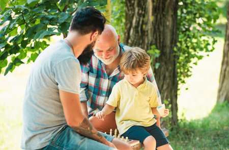 Cute boy developing chess strategy. Father son and grandfather relaxing together. Golden age...