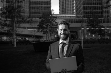 Businessman with notebook outdoor. Confident business expert. Handsome man in suit holding laptop against office background.の写真素材