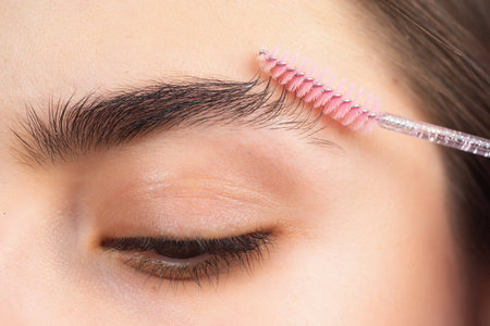 Eyebrow shaping. Close up of woman getting eyebrow make-up. Macro of combing eyebrows. Perfect shape of eyebrow, brown eyeshadows and long eyelashes. Girl with beauty shape eyebrows.の写真素材