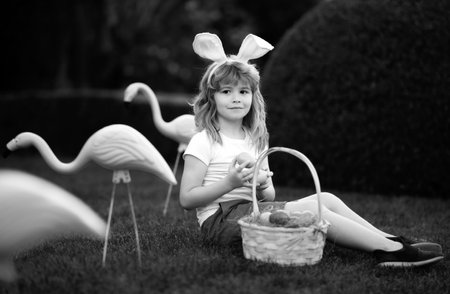 Easter egg hunt. Easter bunny boy. Child in bunny ears hunting easter eggs outdoor on backyard.の写真素材