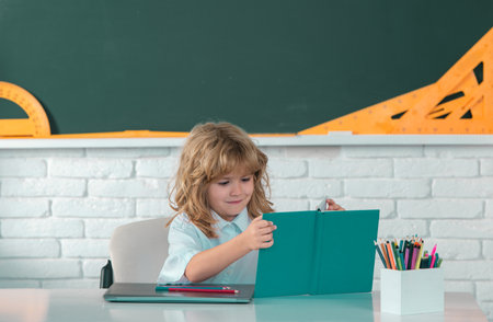 Cute little school kid boy read book in a classroom.