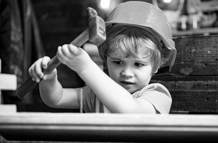 Kid in hard hat holding wooden plank and hammer. Child engineer with carpenter work hammer on wood.の写真素材