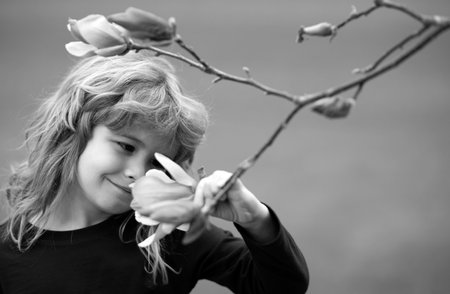 Little child is smelling flowers on green backyard. Adorable kid on a summer meadow and smelling flowers. Summer fun for family with kids outdoors in a beautiful spring garden.の写真素材