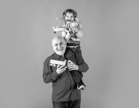 Grandfather and grandson piggyback with toy plane and wooden truck. Men generation granddad and grandchild.の写真素材