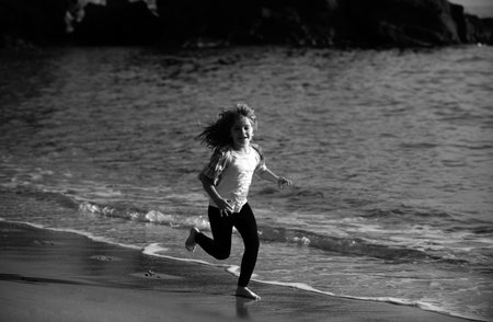 Happy kid running on sea beach. Funny boy run along surf edge. Active kids lifestyle. Run and healthy sport for children.の写真素材