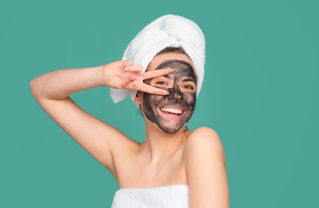 Mud facial mask, face clay mask spa. Funny amazed woman with cosmetic mud facial procedure, spa health concept. Skin care beauty treatment. Towel on head. Medical mineral mud.の写真素材