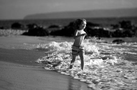Happy boy running beach near the seaside. Excited amazed kid having fun with running through water in ocean or sea.の写真素材