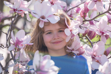 Spring fun for kids. Child play outdoors in a beautiful spring garden. Kid face in flowers. Adorable...