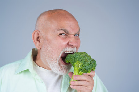 Funny Senior on Diet. Broccoli. Old mature man eating Broccoli. Healthy food, dieting for Seniors. Mature man bite broccoli in studio. Vegan man. Aged Dieting. Healthy food. Broccoli for weight loss.の写真素材