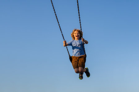 Joyful kid swinging on a swing. Happiness children. Child extreme swinging. Danger high Swing in sky. Craziness and freedom. Kid playing on swing-set outdoor. Playful child swinging very high to the sky.の写真素材