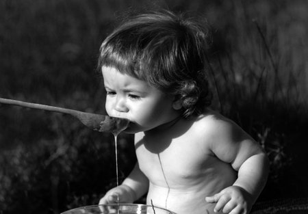 Feeding baby. Cute toddler baby eating healthy food. Feed with spoon outdoor on green grass.の写真素材