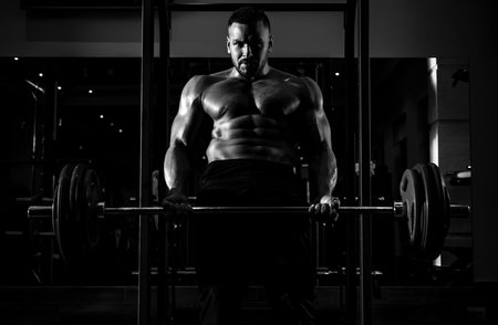 Muscular man doing crossfit. Muscular man doing biceps lifting barbell. Young man working out at crossfit gym. Athletic guy doing exercise.の写真素材